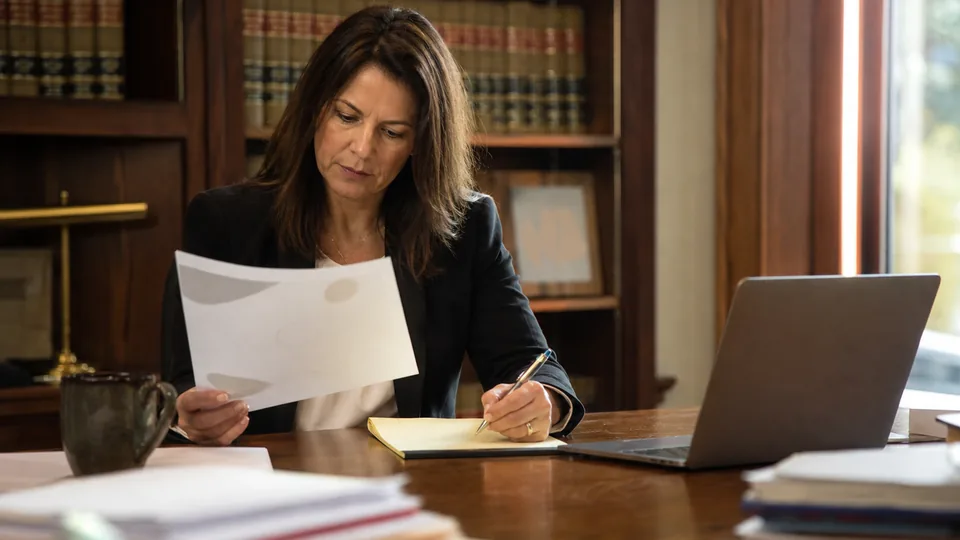 Attorney at her desk comparing a printed software quote with handwritten notes beside a laptop