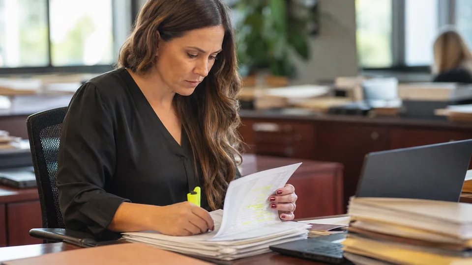 Paralegal at a personal injury firm reviewing a stack of medical records and bills next to a laptop